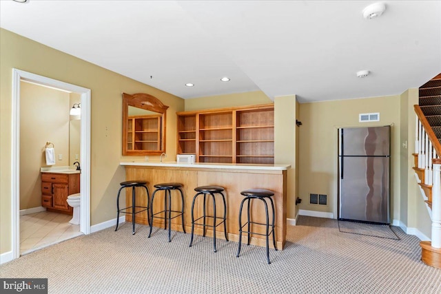 kitchen with light colored carpet, stainless steel fridge, kitchen peninsula, and a breakfast bar area