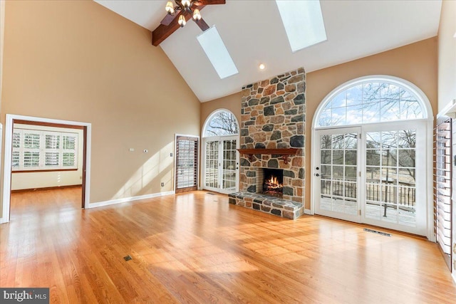 unfurnished living room featuring hardwood / wood-style flooring, ceiling fan, beam ceiling, a skylight, and a fireplace