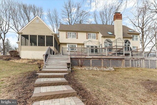 rear view of property featuring a wooden deck, a lawn, and a sunroom