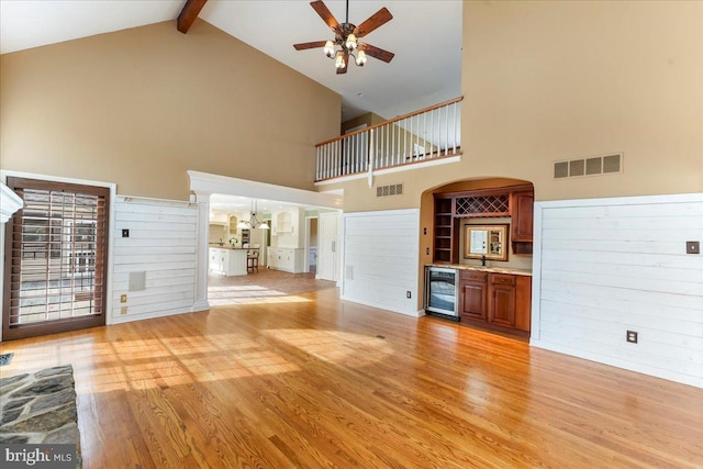 unfurnished living room with bar area, beverage cooler, ceiling fan, and light hardwood / wood-style flooring