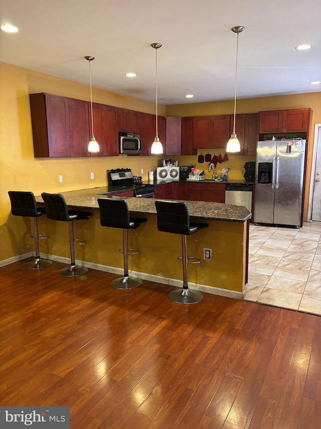 kitchen with a kitchen breakfast bar, stainless steel appliances, dark stone counters, and light hardwood / wood-style flooring