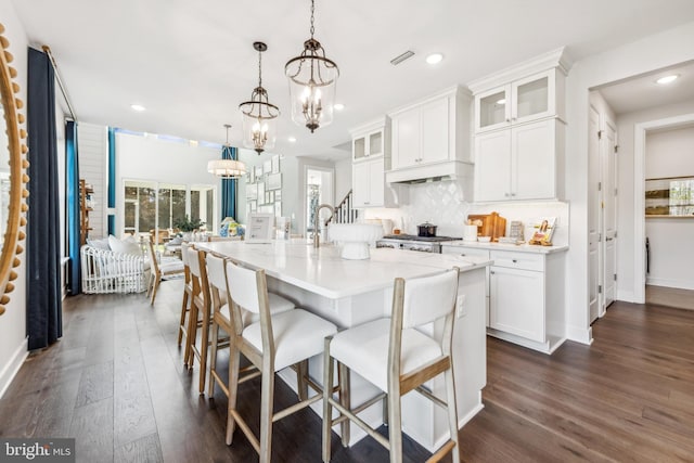 kitchen with white cabinets, decorative light fixtures, an island with sink, and dark wood-type flooring