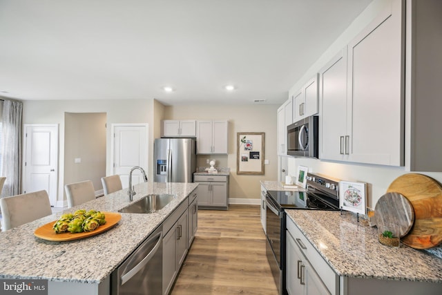 kitchen featuring sink, light stone counters, an island with sink, light hardwood / wood-style floors, and appliances with stainless steel finishes