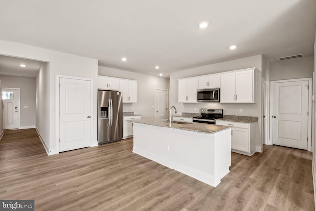 kitchen featuring light wood-type flooring, stainless steel appliances, white cabinetry, and a center island with sink