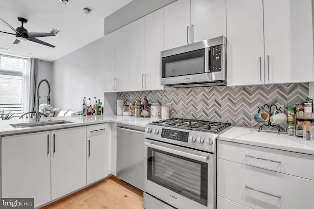 kitchen with white cabinets, sink, ceiling fan, light wood-type flooring, and stainless steel appliances