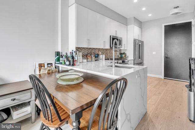 kitchen with backsplash, kitchen peninsula, appliances with stainless steel finishes, light hardwood / wood-style floors, and white cabinetry