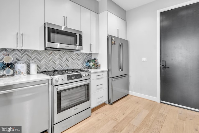 kitchen with backsplash, white cabinets, stainless steel appliances, and light hardwood / wood-style floors