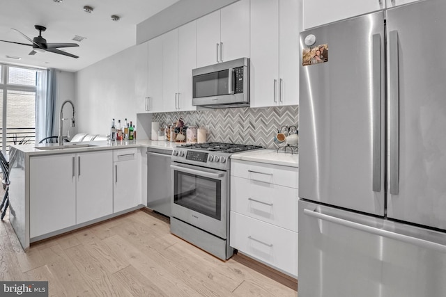 kitchen featuring white cabinets, light hardwood / wood-style flooring, ceiling fan, kitchen peninsula, and stainless steel appliances