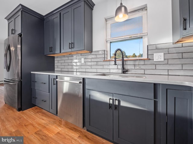 kitchen with pendant lighting, backsplash, sink, light hardwood / wood-style flooring, and appliances with stainless steel finishes