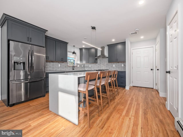 kitchen featuring wall chimney exhaust hood, stainless steel fridge with ice dispenser, pendant lighting, a kitchen island, and light wood-type flooring