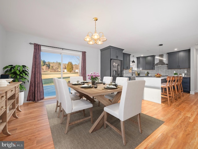 dining area with sink, an inviting chandelier, and light wood-type flooring