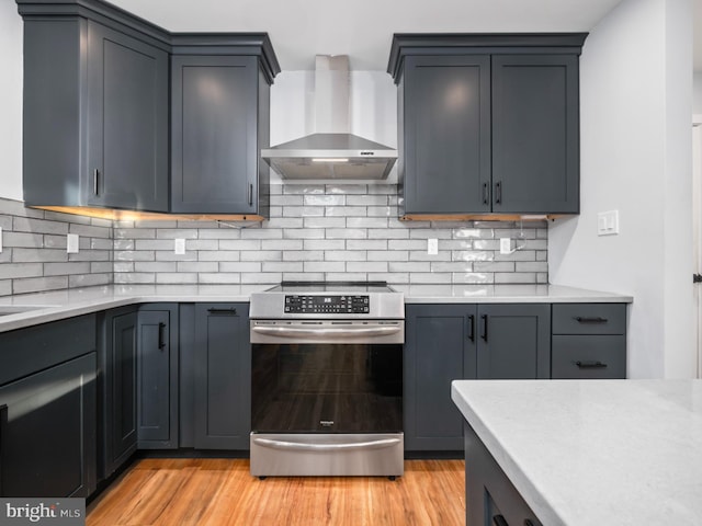 kitchen with stainless steel range, backsplash, light hardwood / wood-style floors, and wall chimney exhaust hood