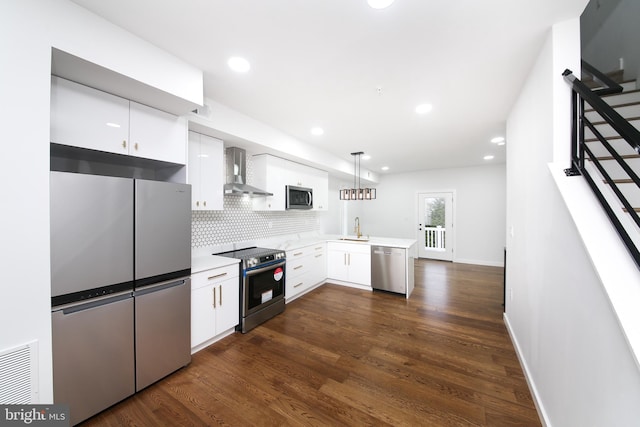 kitchen featuring white cabinets, stainless steel appliances, hanging light fixtures, and wall chimney range hood