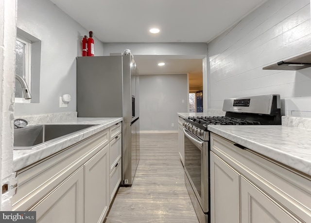 kitchen with light stone countertops, appliances with stainless steel finishes, sink, light hardwood / wood-style floors, and white cabinetry