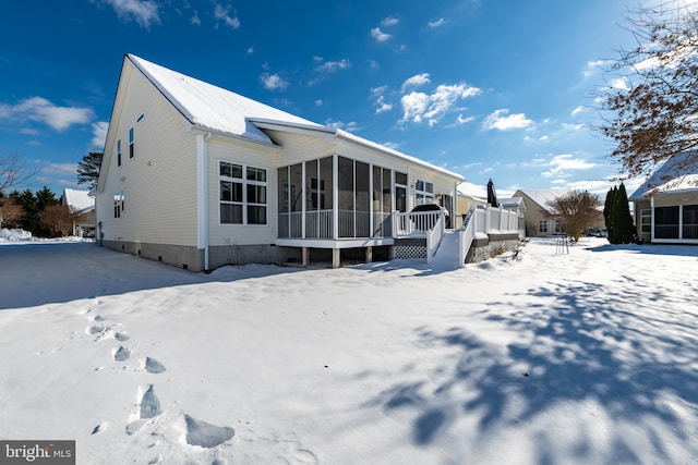 snow covered back of property with a sunroom