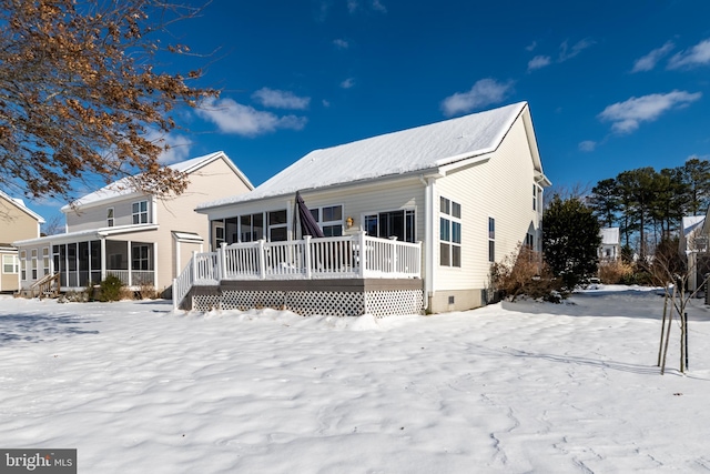 snow covered rear of property featuring a deck and a sunroom