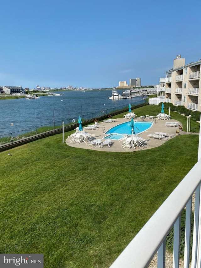 view of swimming pool featuring a water view, a patio area, and a lawn