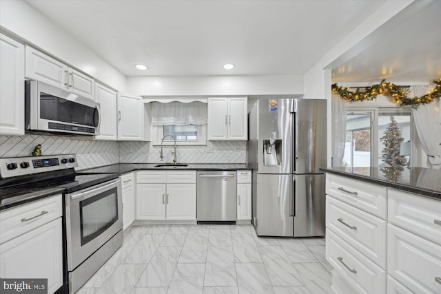 kitchen featuring backsplash, dark stone counters, white cabinets, sink, and stainless steel appliances