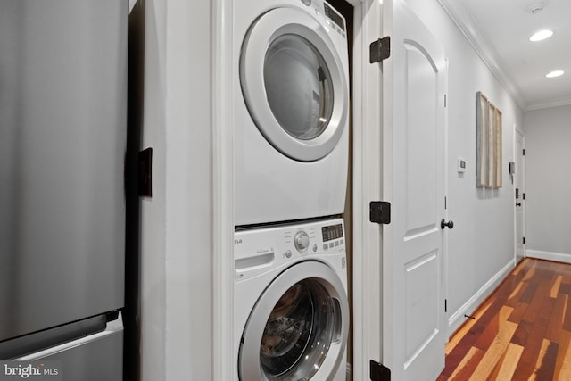 clothes washing area with stacked washing maching and dryer, ornamental molding, and dark wood-type flooring