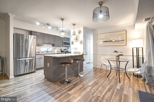 kitchen with a kitchen breakfast bar, light stone counters, stainless steel appliances, light hardwood / wood-style flooring, and hanging light fixtures