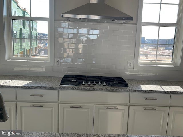 kitchen with white cabinets, a healthy amount of sunlight, and wall chimney range hood