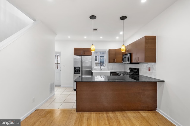 kitchen with kitchen peninsula, appliances with stainless steel finishes, light wood-type flooring, sink, and hanging light fixtures