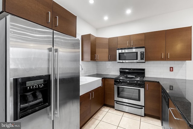 kitchen featuring dark stone countertops, decorative backsplash, light tile patterned flooring, and stainless steel appliances