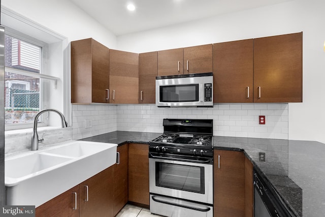 kitchen with tasteful backsplash, dark stone counters, stainless steel appliances, sink, and light tile patterned floors