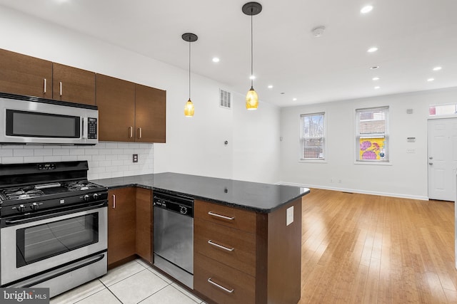 kitchen featuring pendant lighting, light wood-type flooring, tasteful backsplash, kitchen peninsula, and stainless steel appliances