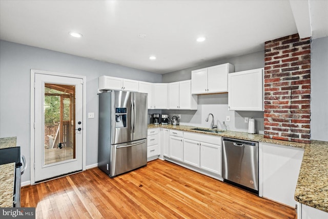 kitchen featuring light wood-type flooring, light stone counters, stainless steel appliances, sink, and white cabinetry