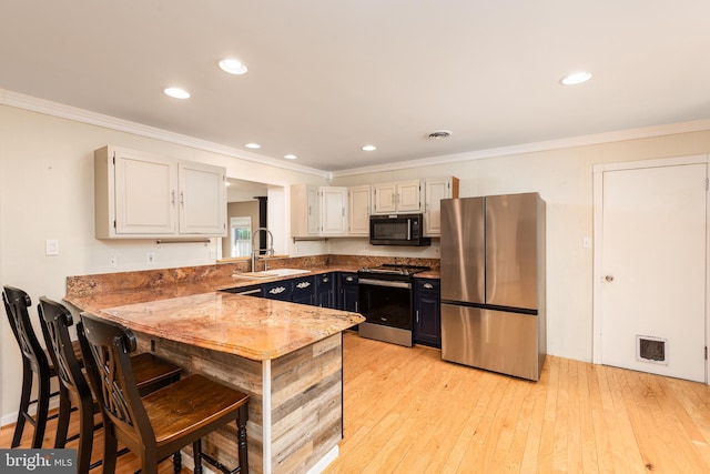 kitchen with ornamental molding, appliances with stainless steel finishes, a sink, and light wood-style floors