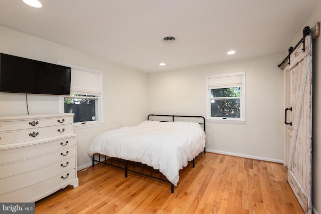 bedroom with a barn door and light hardwood / wood-style floors