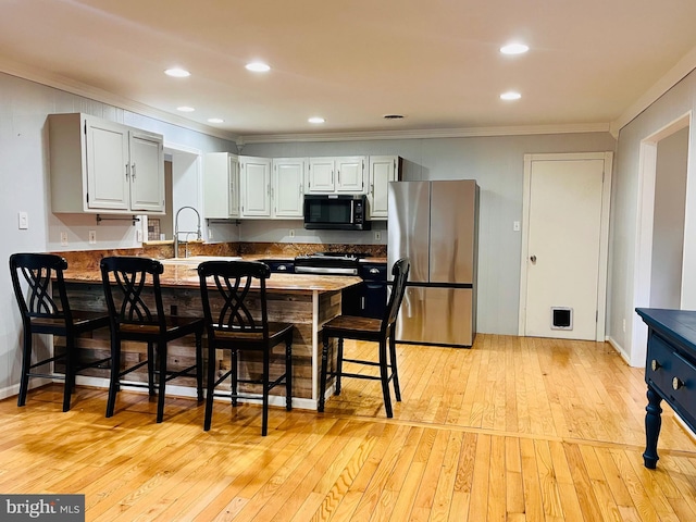 kitchen featuring light wood finished floors, ornamental molding, freestanding refrigerator, black microwave, and a sink