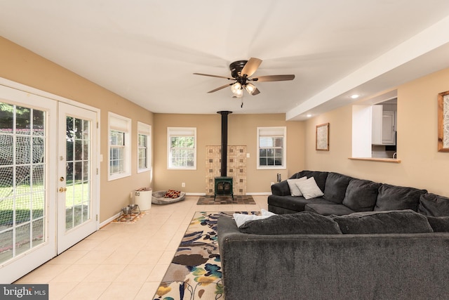 living area featuring light tile patterned floors, baseboards, a ceiling fan, a wood stove, and french doors