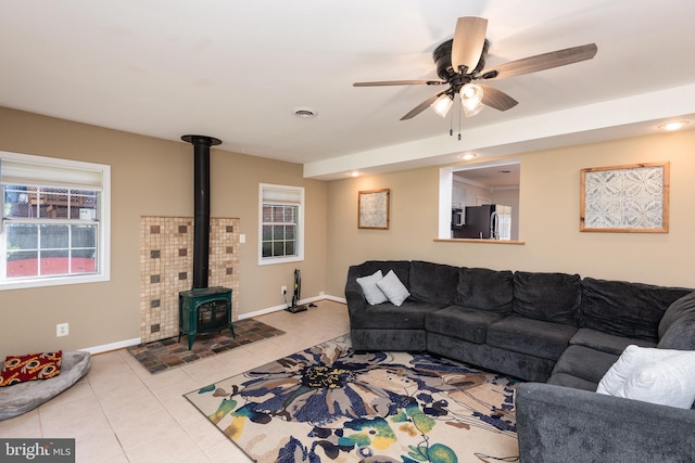 tiled living room featuring a wood stove and ceiling fan