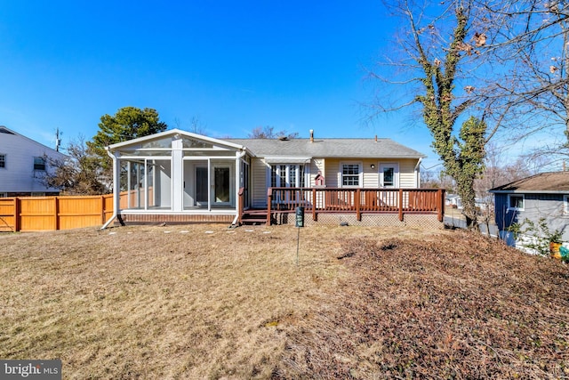 rear view of house with a sunroom, fence, a deck, and a lawn