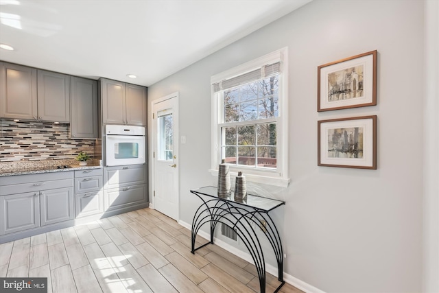 kitchen with oven, wood finish floors, baseboards, backsplash, and gray cabinets