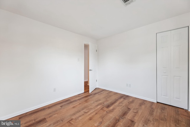 unfurnished bedroom featuring baseboards, a closet, visible vents, and wood finished floors