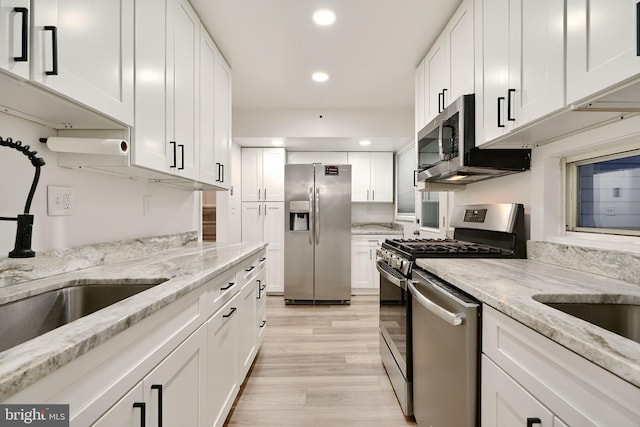 kitchen featuring white cabinetry, light hardwood / wood-style flooring, light stone counters, and appliances with stainless steel finishes