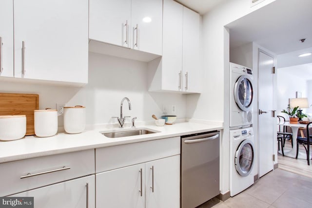 kitchen featuring stacked washing maching and dryer, white cabinets, sink, dishwasher, and light tile patterned flooring