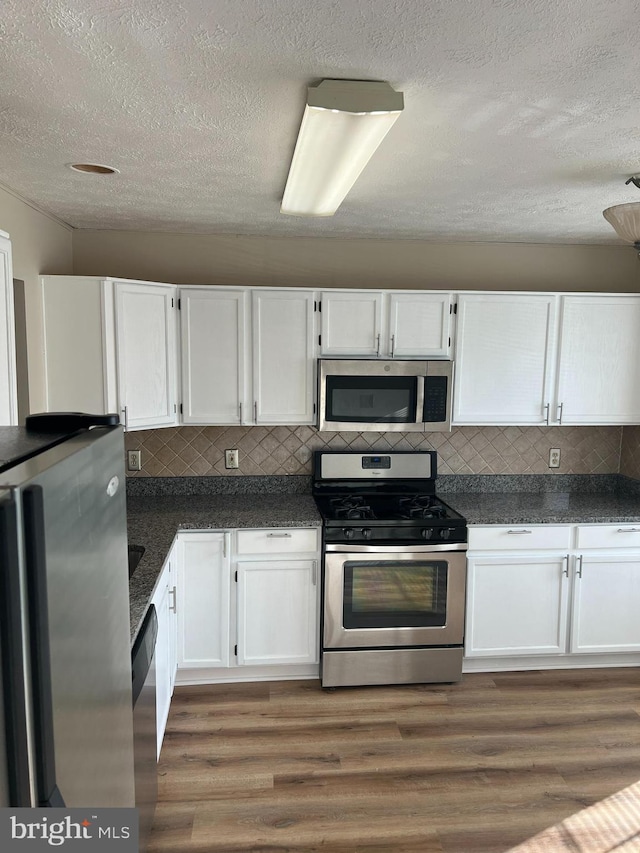 kitchen with white cabinets, dark countertops, stainless steel appliances, and wood finished floors