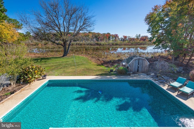 view of pool with a yard, a water view, and a storage unit