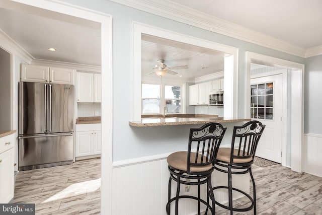 kitchen with light stone countertops, stainless steel appliances, a breakfast bar, white cabinets, and ornamental molding