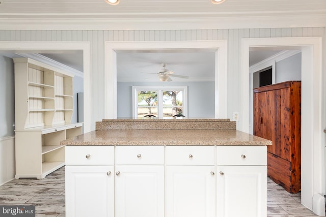 kitchen with light stone countertops, white cabinets, ceiling fan, and ornamental molding