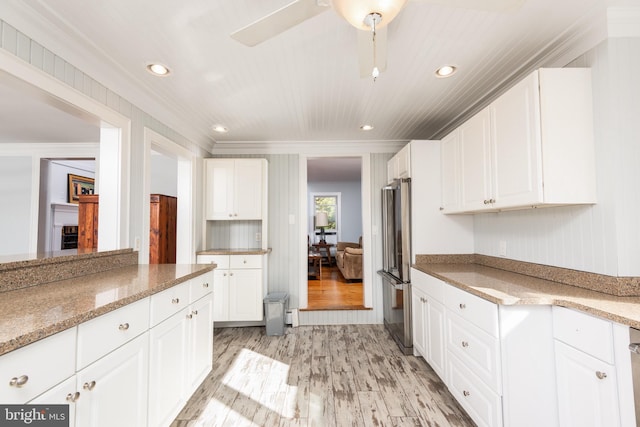 kitchen featuring white cabinets, stainless steel fridge, light stone countertops, light wood-type flooring, and ornamental molding