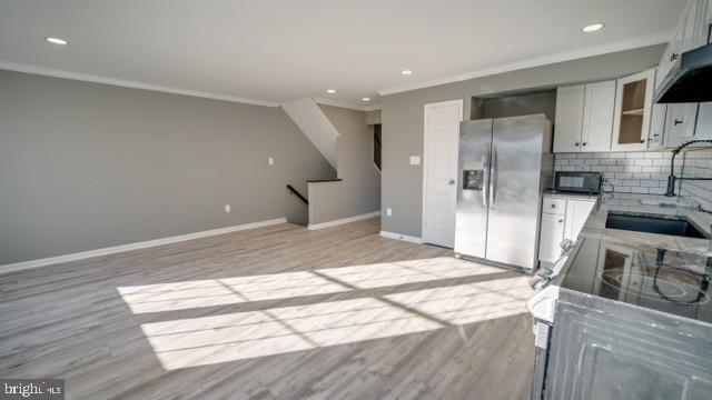 kitchen featuring white cabinetry, sink, stainless steel fridge with ice dispenser, light hardwood / wood-style flooring, and ornamental molding