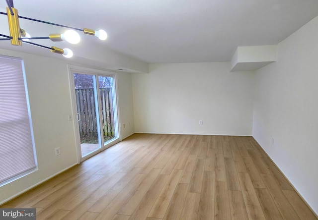 empty room featuring light wood-type flooring and a notable chandelier