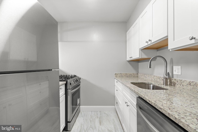 kitchen featuring white cabinets, appliances with stainless steel finishes, light stone counters, and sink