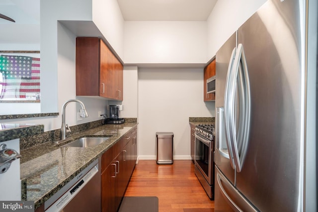 kitchen with appliances with stainless steel finishes, light hardwood / wood-style flooring, dark stone counters, and sink