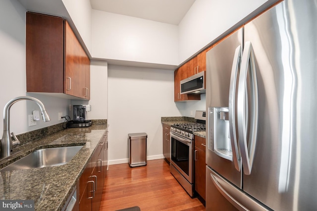 kitchen featuring dark stone counters, sink, appliances with stainless steel finishes, and light hardwood / wood-style flooring